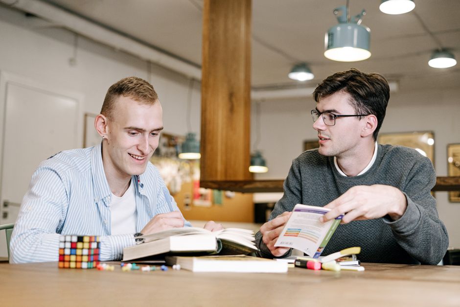 Two young men study together at a table,